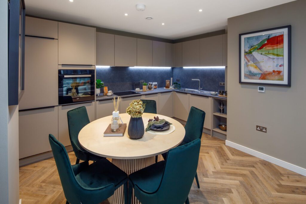 A kitchen with full appliances, green dining chairs, dining table and wall painting.