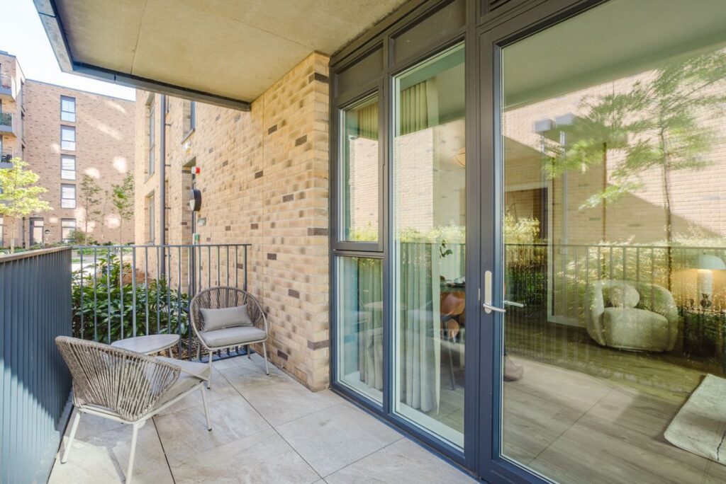 Balcony with Grey windows and a door. Railings and two beige chairs with a small table